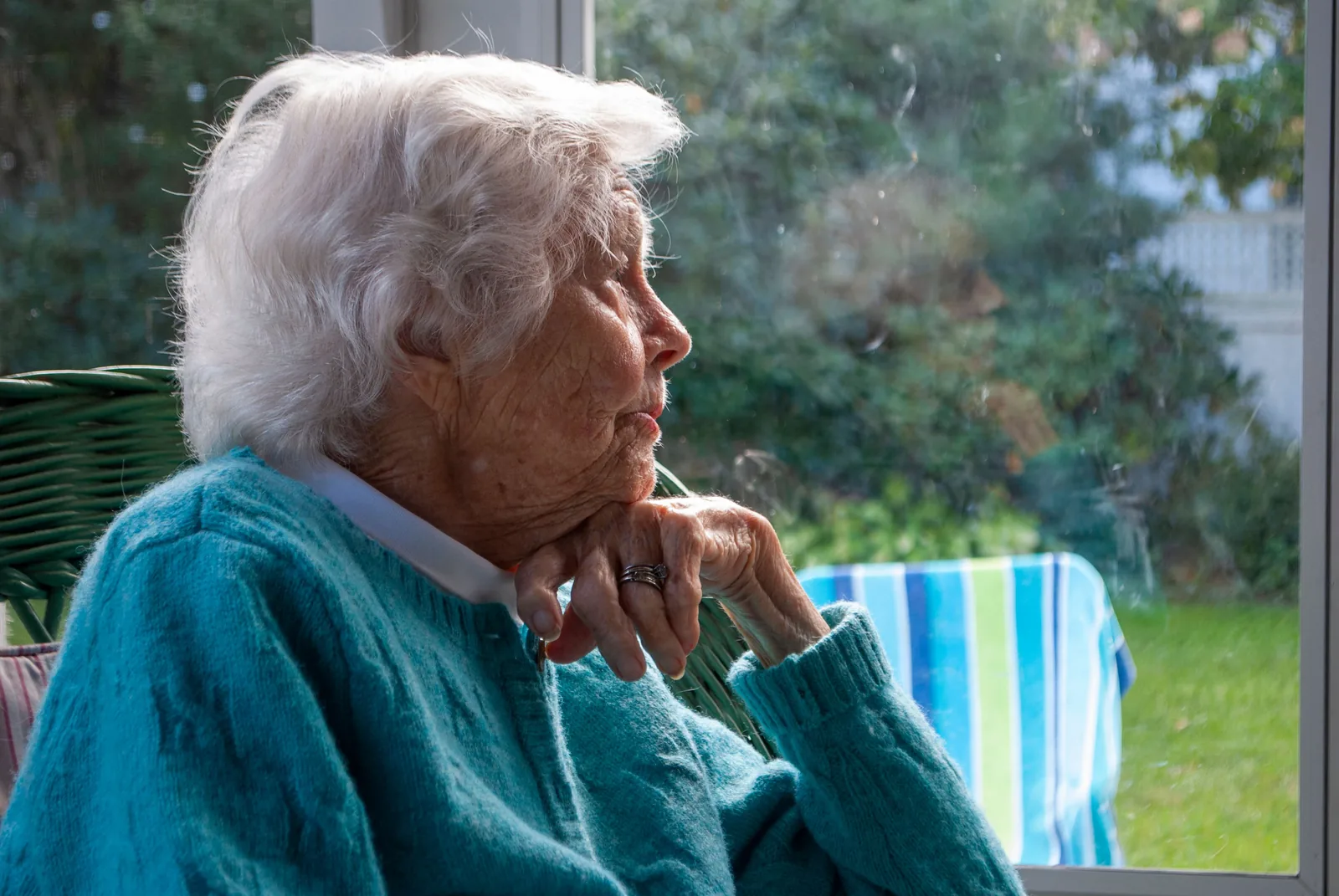 A senior woman resting by a sunlit window at home, looking outside in quiet reflection